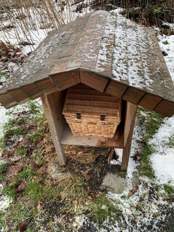 Ein Henkelkorb steht in einer kleinen Hütte am Fuß der Treppe zum Baumhaus.