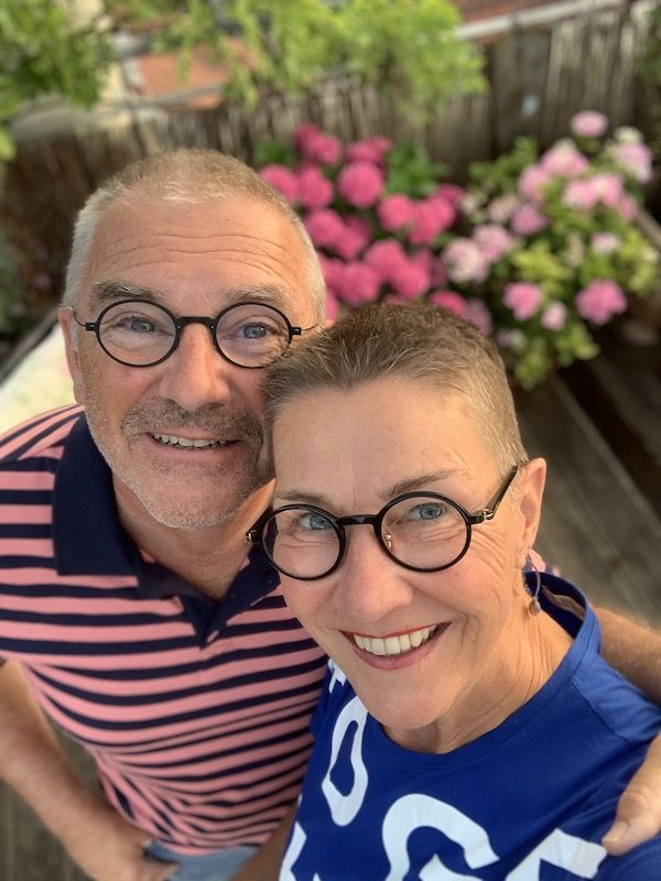 Profilbild von Elke Schulz, Inhaberin der Kommunikationskochschule, und ihrem Mann Uli. Beide lachen in die Kamera. Im Hintergrund zwei pink und rosa blühende Hortensien.