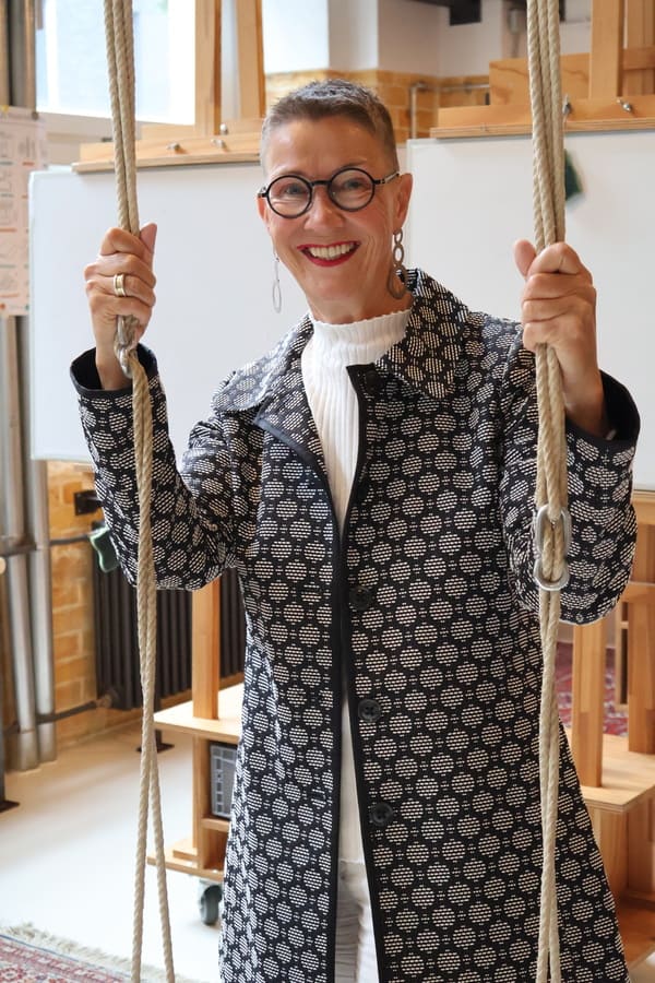 Portraet-von-Elke-Schulz-4 Elke Schulz mit gemustertem Mantel steht hinter einer Schaukel und hält sich an den Seilen fest
